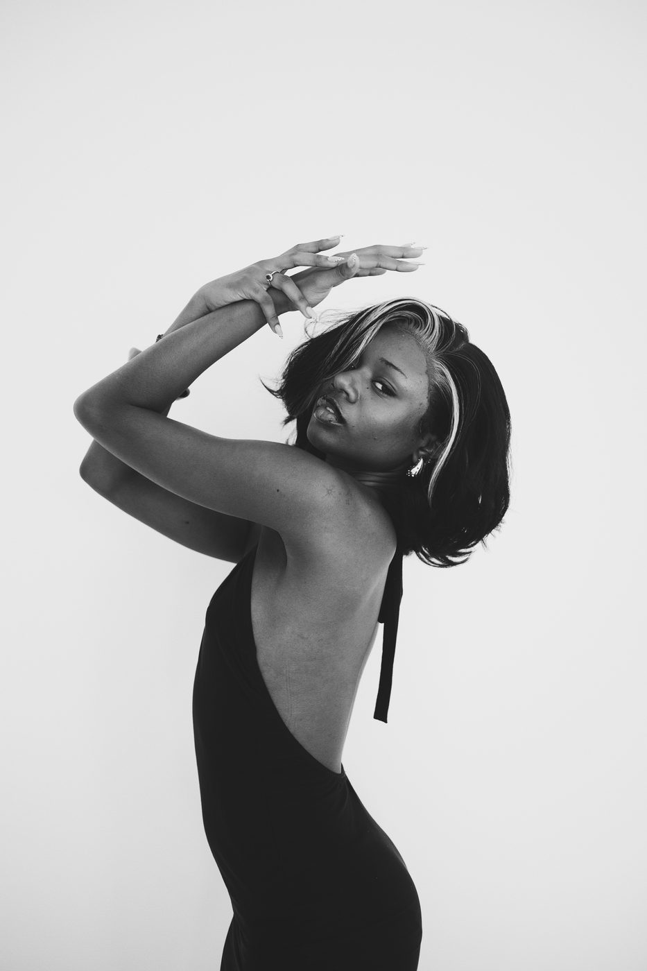 Black and white portrait of a woman in a backless dress, arms raised above her head